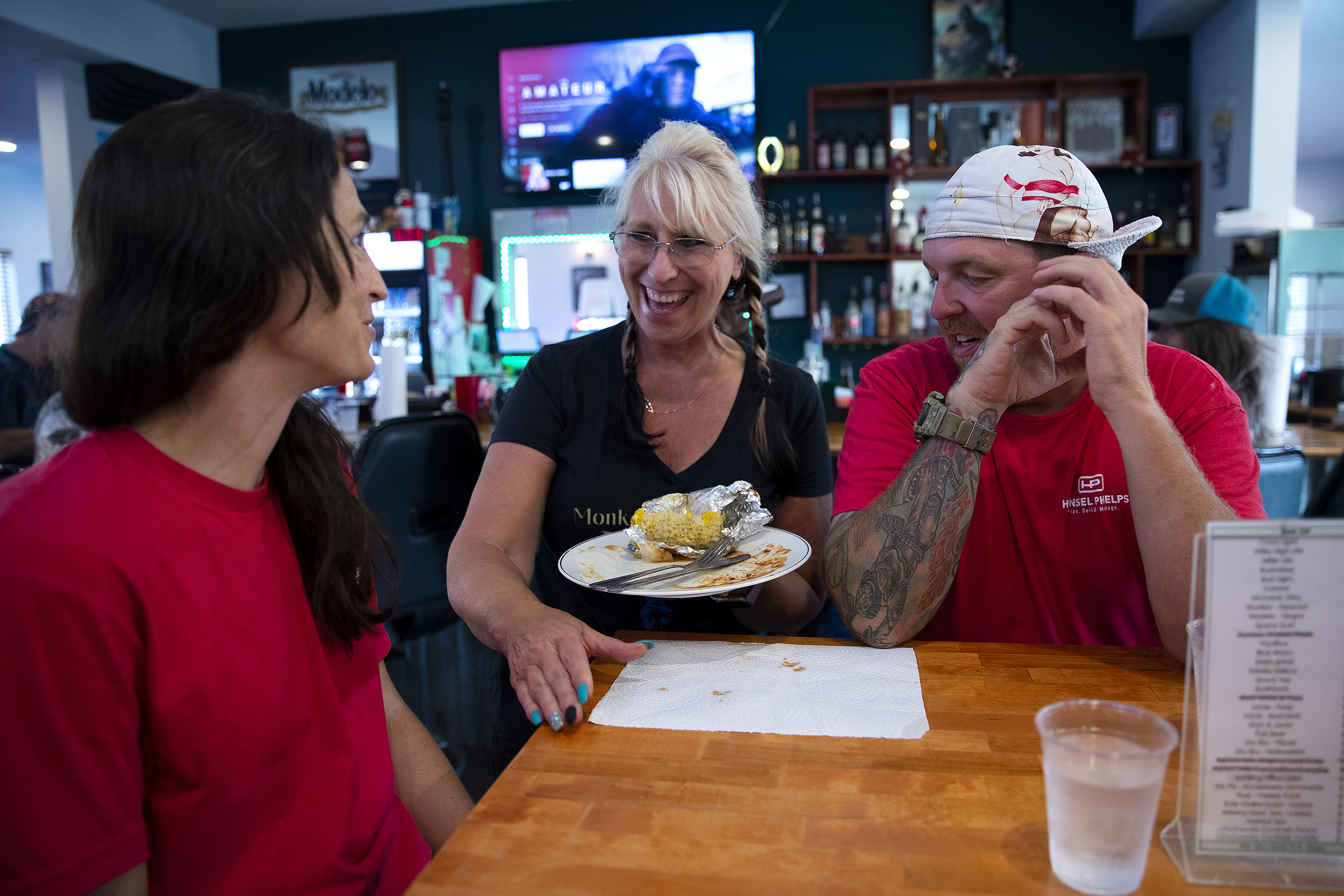 caption: Sharyl Smith, center, owner of Monkey N’Around Pizza, laughs with electricians Micki Bohman, left, and Mark Gruszkiewicz, right, during IBEW Brotherhood Night on Thursday, July 17, 2025, in Quincy, Washington. Bohman and Gruszkiewicz met at a data center job site and got married a year and a half ago. 