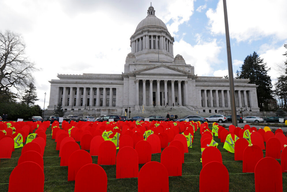 caption: Red mock tombstones represent the more than 1,000 people who took their lives by suicide in Washington state in 2017, displayed Tuesday, March 12, 2019 at the Capitol in Olympia. The yellow vests on some of the markers indicate the victim was from the construction industry, and similar markers were used to designate youth and military veterans. 