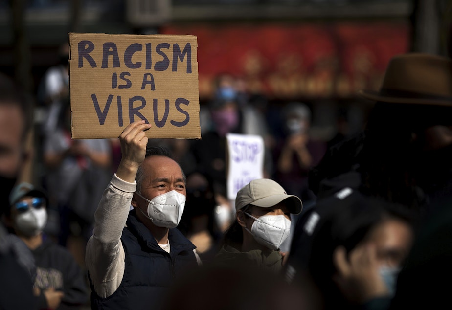 caption: Michael Lee holds a sign in the air that reads 'Racism Is a Virus,' as hundreds gathered for the 'We Are Not Silent' rally and march against anti-Asian hate and violence on Saturday, March 13, 2021, at Hing Hay Park in Seattle. Several days of actions are planned by rally organizers in the Seattle area following recent attacks and violence against Asian American and Pacific Islander communities.