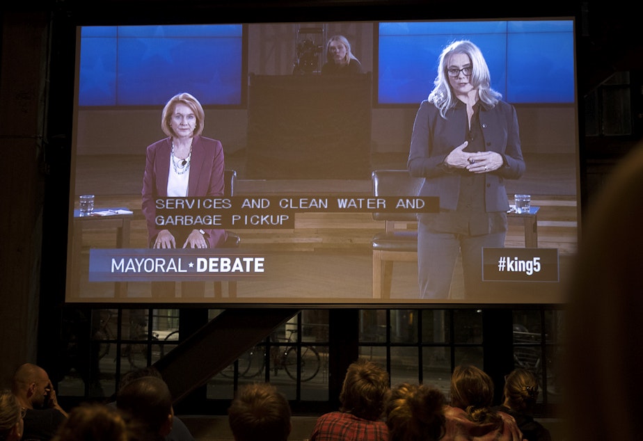 caption: Mayoral candidates Jenny Durkan, left, and Cary Moon are shown on a screen during a mayoral debate viewing party on Tuesday, October 24, 2017, at Optimism Brewing Company in Seattle.