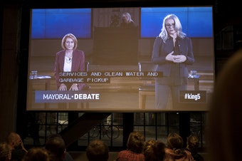 caption: Mayoral candidates Jenny Durkan, left, and Cary Moon are shown on a screen during a mayoral debate viewing party on Tuesday, October 24, 2017, at Optimism Brewing Company in Seattle.
