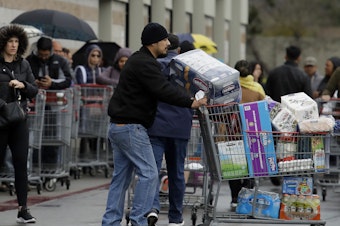 caption: Costco customers roll groceries to their cars as others wait to enter the store on Saturday, March 14, 2020, in San Leandro, Calif.