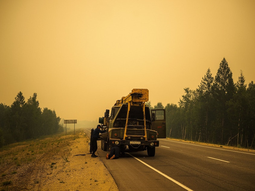 caption: Men repair their truck in smoke from a forest fire on a road near Magaras, in the republic of Sakha, Siberia, in July.