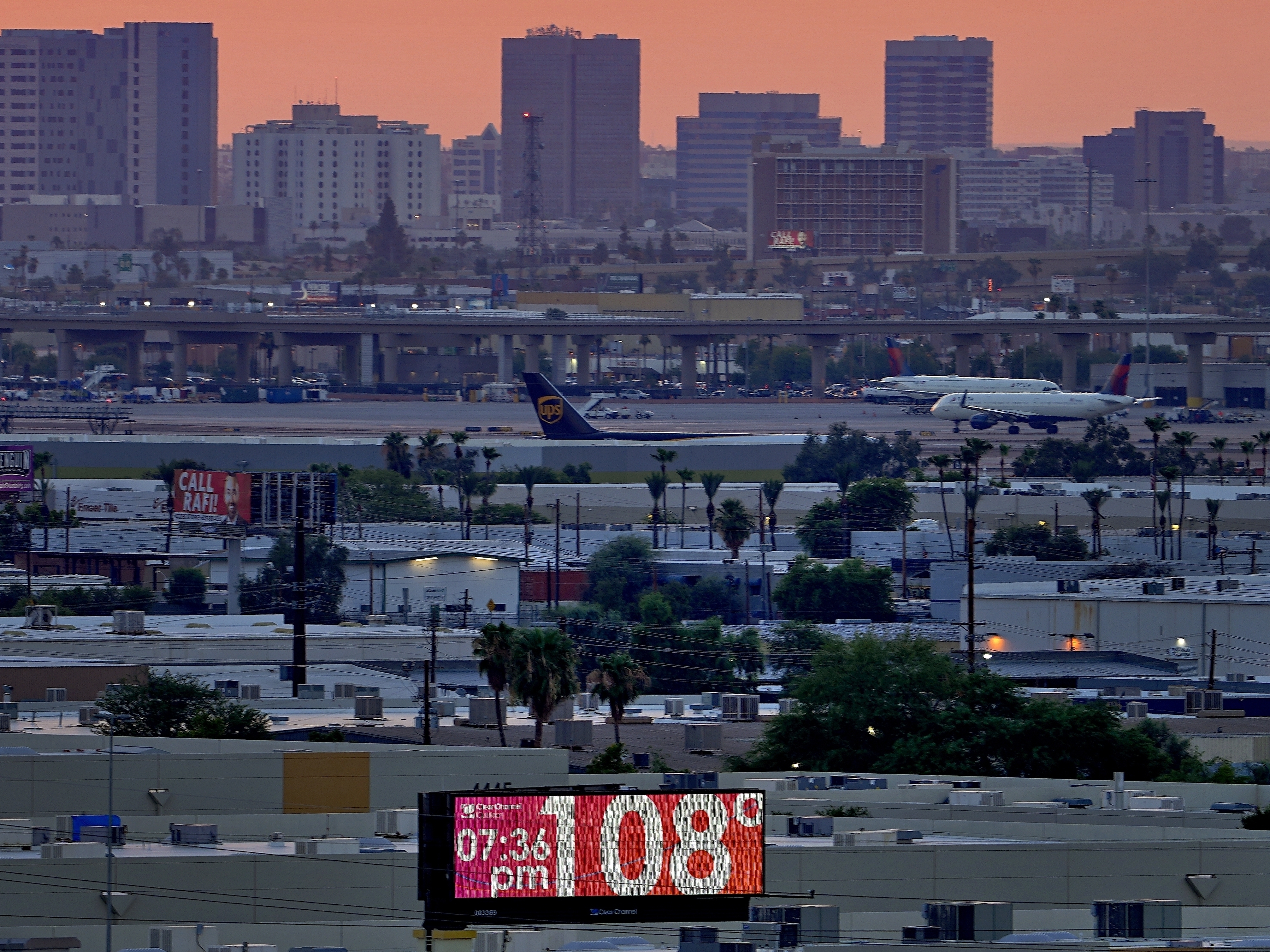 caption: A sign displays an an unofficial temperature as jets taxi at Sky Harbor International Airport at dusk, July 12 in Phoenix.
