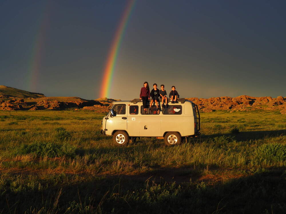 caption: Mia, Leo, Colin, and Laurent Pelletier pose on top of their camper van in front of a
double rainbow while in Mongolia.
(Credit: Edith Lemay)
