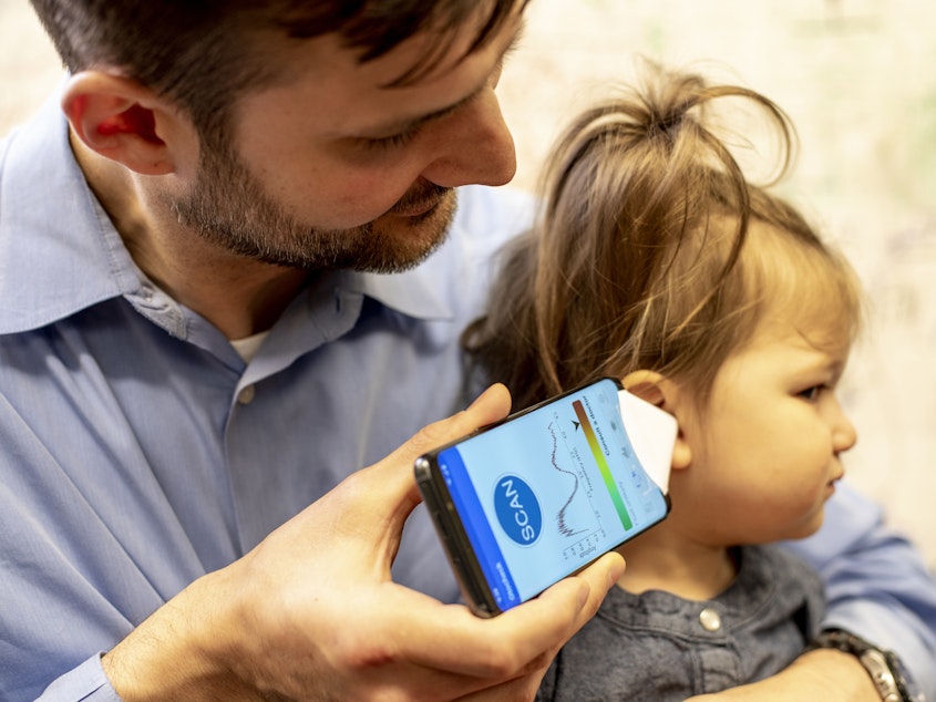 caption: Dr. Randall Bly, an assistant professor of otolaryngology-head and neck surgery at the University of Washington School of Medicine who practices at Seattle Children's Hospital, uses the experimental smartphone app and a paper funnel to check his daughter's ear.