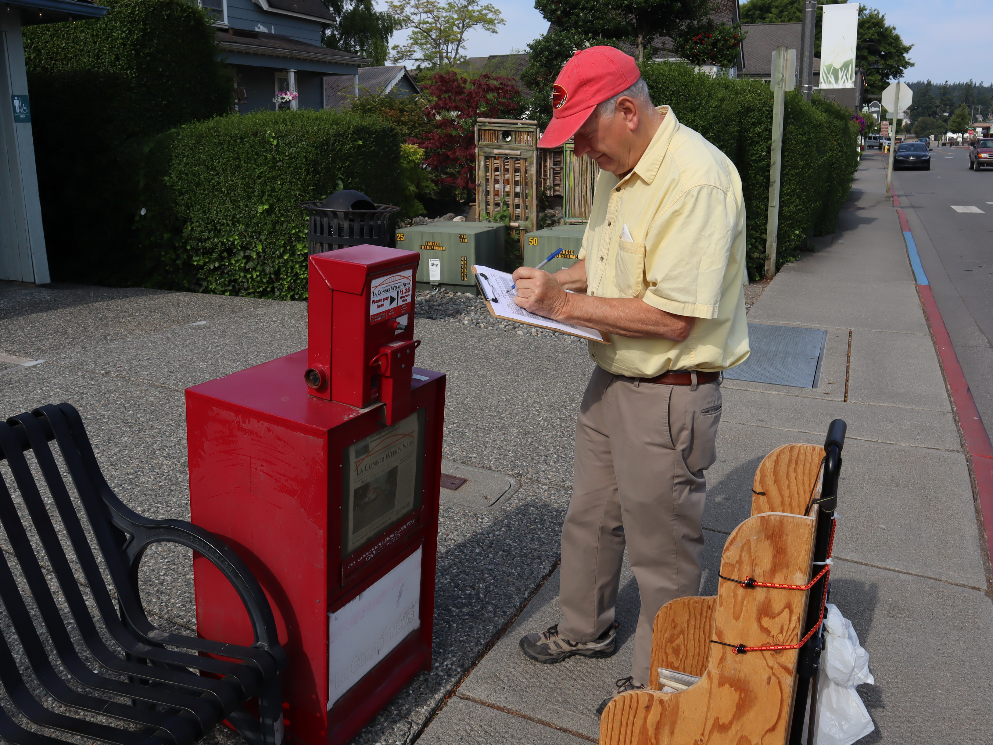 caption: La Conner Weekly News' editor and publisher Ken Stern uses a clipboard to track how many copies of the weekly paper are sold at the different stops around town, including newspaper boxes, the local grocery store, and several coffee shops nearby. He says he's noticed a decline in the number of papers sold from the boxes over the years but wants to keep them available to people walking throughout town. 