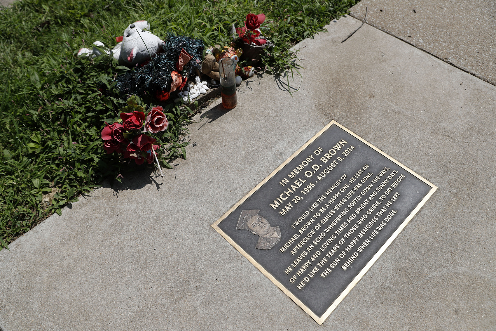 caption: In this July 25, 2019, photo, flowers and other items lay near a memorial plaque in the sidewalk near the spot where Michael Brown was shot and killed by a police officer five years ago in Ferguson, Mo. (Jeff Roberson/AP)