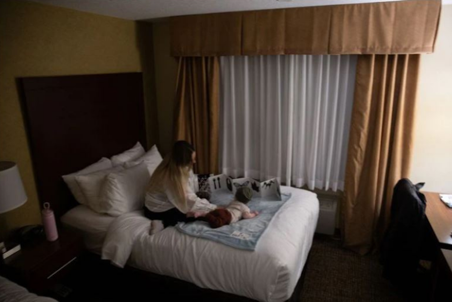 caption: Claire and her 5-month-old son play on a bed at a Comfort Inn and Suites near downtown Vancouver. Claire spent three weeks living out of the hotel as she tried to get her husband help during a mental health break.