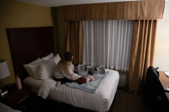caption: Claire and her 5-month-old son play on a bed at a Comfort Inn and Suites near downtown Vancouver. Claire spent three weeks living out of the hotel as she tried to get her husband help during a mental health break.