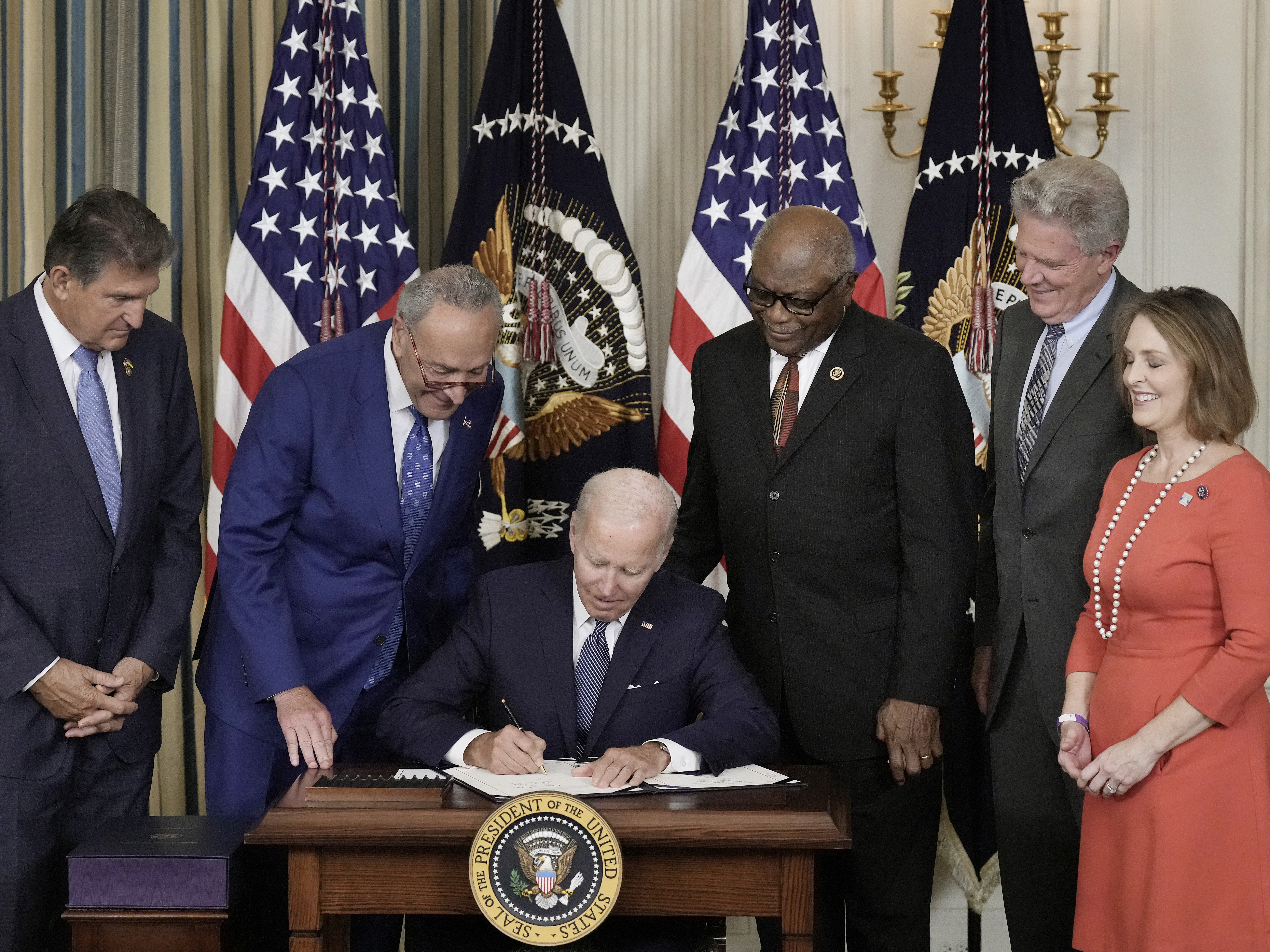 caption: President Joe Biden (C) signs The Inflation Reduction Act with (L-R) Sen. Joe Manchin (D-WV), Senate Majority Leader Charles Schumer (D-NY), House Majority Whip James Clyburn (D-SC), Rep. Frank Pallone (D-NJ) and Rep. Kathy Catsor (D-FL) in the State Dining Room of the White House August 16, 2022 in Washington, DC.