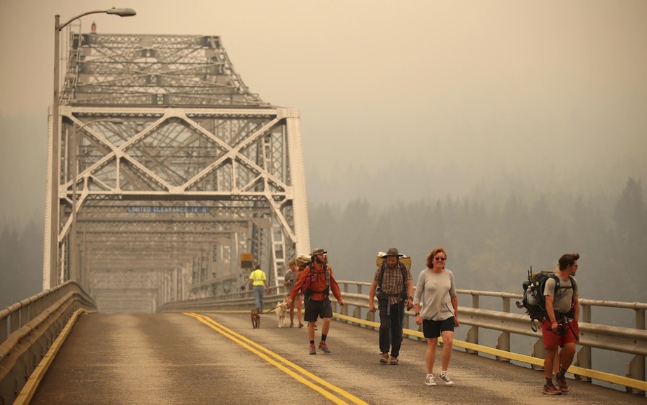 caption: Pedestrians walk off the Bridge of the Gods, which spans the Columbia River between Washington and Oregon, as smoke from the Eagle Creek Fire obscures the Oregon hills in the background near Stevenson, Washington, Wednesday, Sept. 6, 2017. 