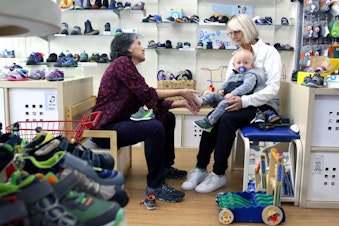 caption: Sarah Stegner (L) helps a customer at her store, Kid Friendly Footwear @ Again and Again. Stegner can't keep employees around due to the high cost of housing.