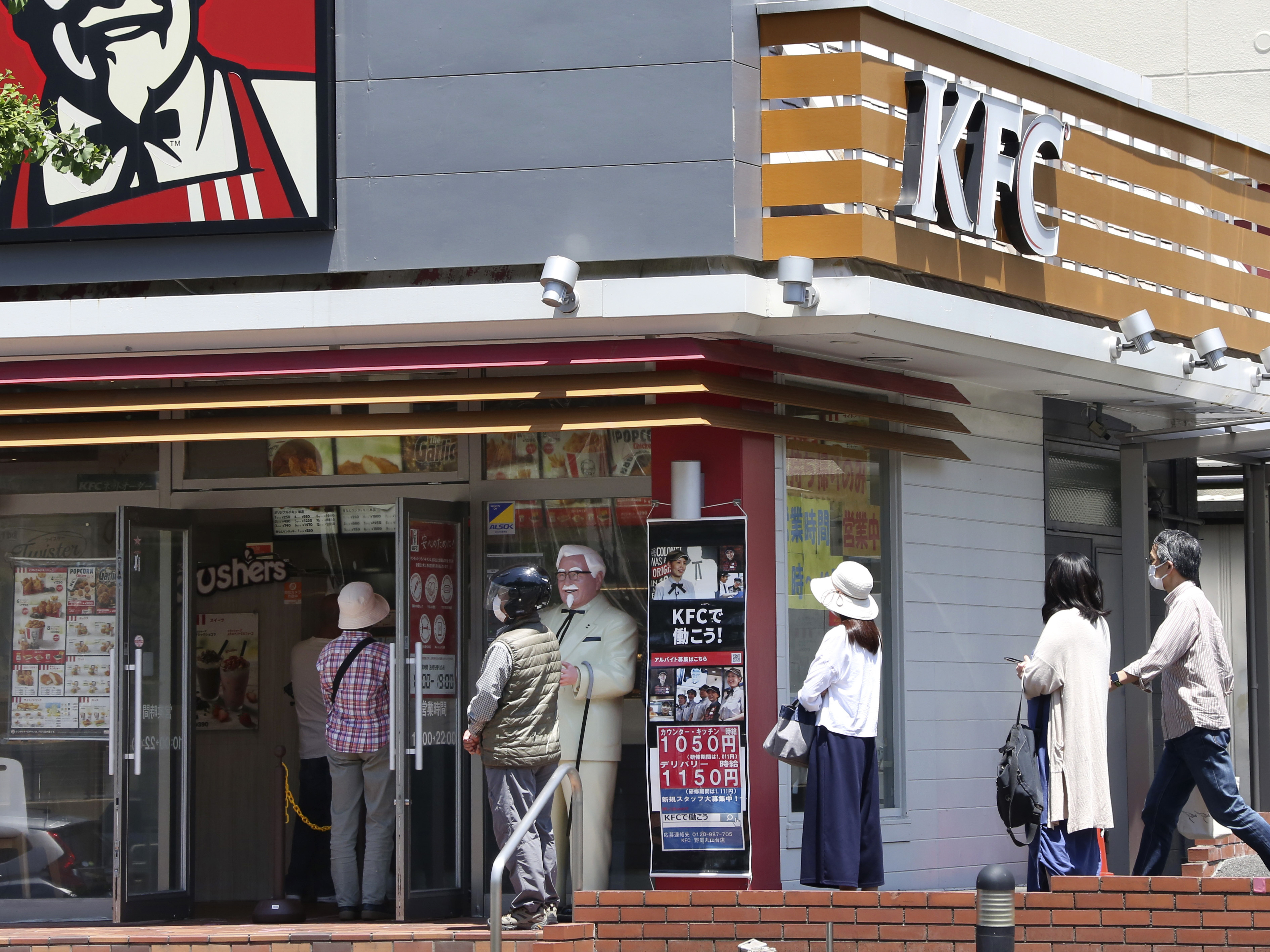 caption: People wearing face masks to protect against the spread of the new coronavirus keep social distancing as they wait to enter a KFC restaurant in Yokohama near Tokyo on May 14, 2020.