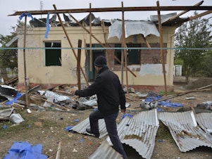 caption: A man walks past a house destroyed by shelling during fighting over Nagorno-Karabakh in Agdam, Azerbaijan, on Oct. 1. The International Committee of the Red Cross says civilian deaths and injuries have been reported.