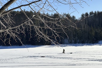 caption: An ice fisherman stands on the frozen Molly's Falls Pond in Marshfield, Vt., on Sunday.