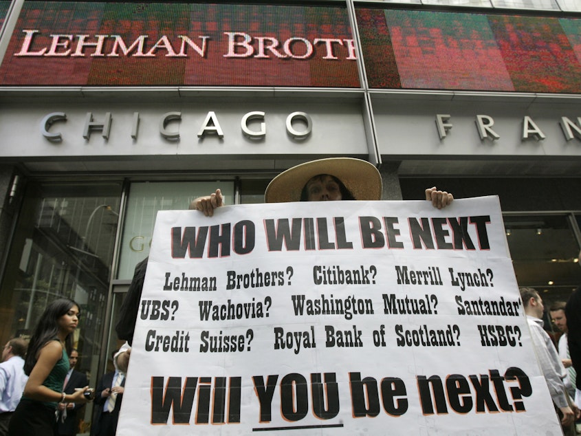 caption: Robin Radaetz holds a sign in front of the Lehman Brothers headquarters Monday, Sept. 15, 2008 in New York. Lehman Brothers filed for Chapter 11 protection in the biggest bankruptcy filing ever at the time and the development was an early part of financial crisis that quickly grew and forced Washington to respond.