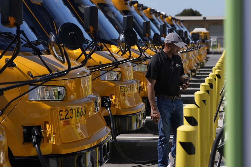 caption: Gaurav Saini, senior program manager of electric vehicles, stands between Zum electric buses and charging stations before a news conference announcing the Oakland Unified School District as being the first major school district in the country to use 100% electric school buses. (Jeff Chiu/AP)
