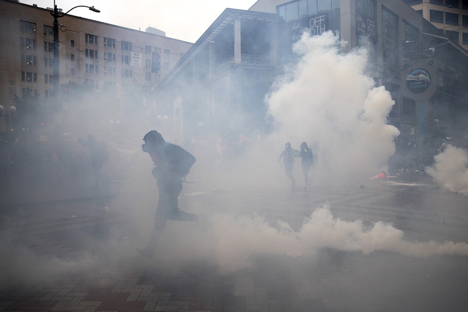 caption: Protesters run through tear gas and flash bombs on Saturday, May 30, 2020, at the intersection of 5th and Pine Streets in Seattle. Thousands gathered in a protest  following the violent police killing of George Floyd, a Black man who was killed by a white police officer who held his knee on Floyd's neck for 8 minutes and 46 seconds, as he repeatedly said, 'I can't breathe,' in Minneapolis on Memorial Day. 