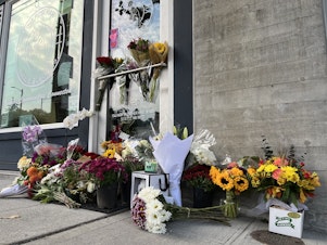 caption: The front of The Postman in Seattle's Central District is lined with flowers Thursday, Oct. 20, following the death of its founder D’Vonne Pickett, Jr. Pickett was shot at a nearby bus stop on Wednesday, Oct. 19. 
