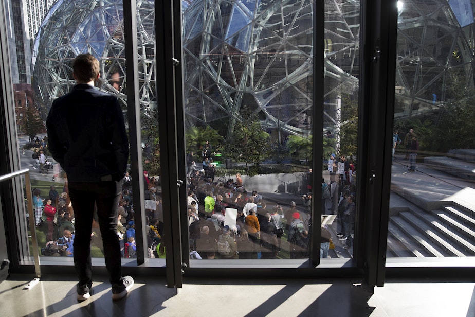 caption: An Amazon employee watches a 'Stop Bezos from Buying this Election rally' on Thursday, October 24, 2019, at Amazon's spheres in Seattle.
