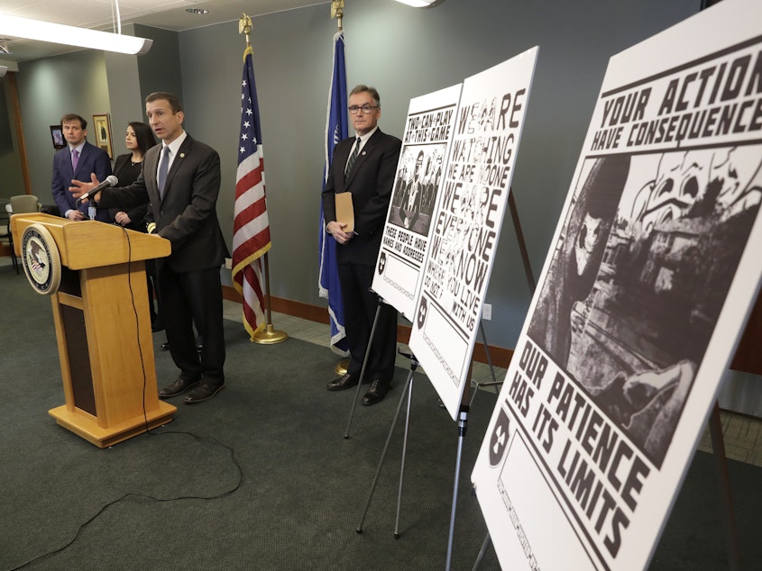 caption: Raymond Duda, FBI Special Agent in Charge in Seattle, speaks in February 2020 about charges against a group of alleged members of the neo-Nazi group Atomwaffen Division for cyber-stalking and mailing threatening communications, including the posters at right, in a campaign against journalists in several cities.