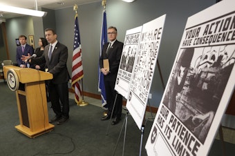 caption: Raymond Duda, FBI Special Agent in Charge in Seattle, speaks in February 2020 about charges against a group of alleged members of the neo-Nazi group Atomwaffen Division for cyber-stalking and mailing threatening communications, including the posters at right, in a campaign against journalists in several cities.