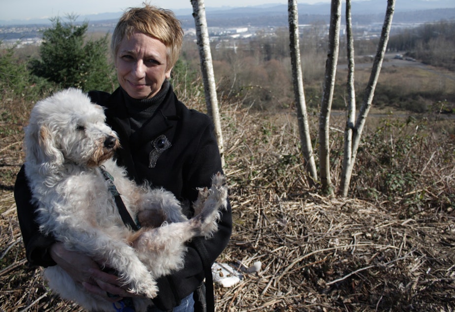 caption: Barbara Dobkin, council of the North Highline Unincorporated Area Council, stands with her dog Mattie on a hill in front of the Seattle city-owned land she'd like to see turned into a park.