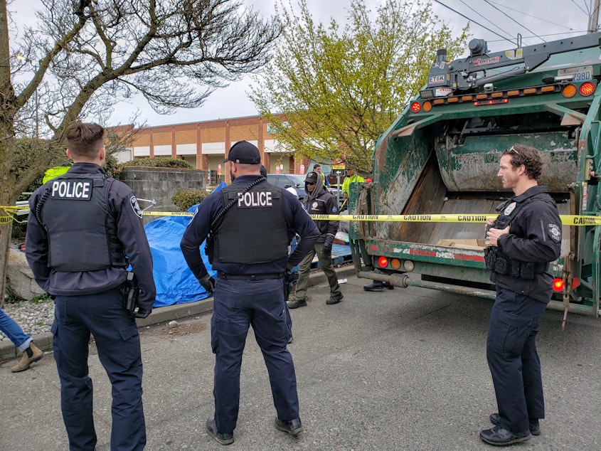 caption: Seattle Police officers watch the removal of a homeless tent encampment in Crown Hill on Thursday, April 14, 2022.