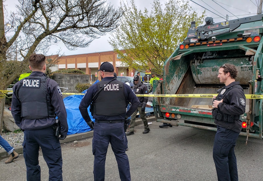 caption: Seattle Police officers watch the removal of a homeless tent encampment in Crown Hill on Thursday, April 14, 2022.
