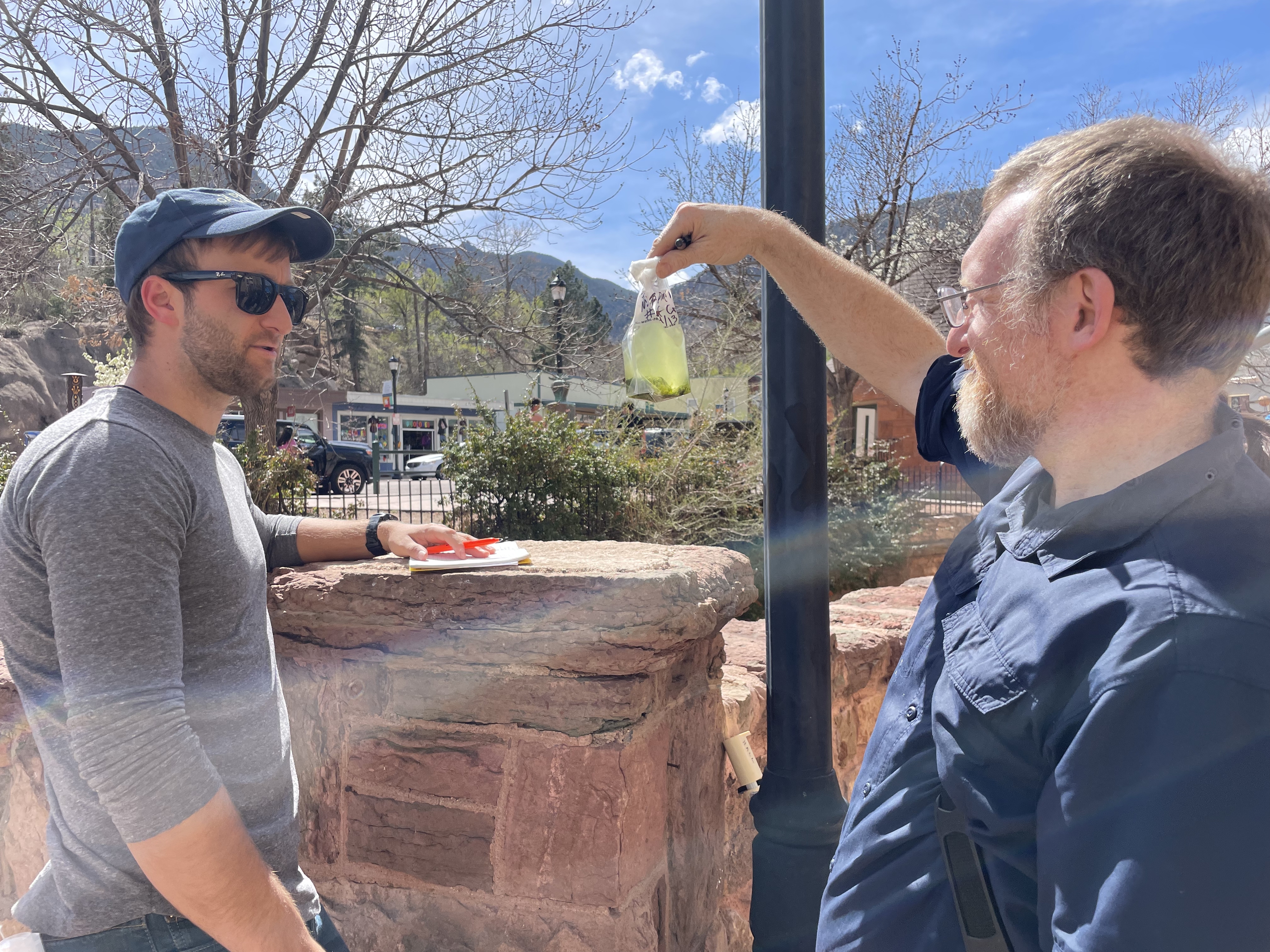 caption: James Henriksen with Colorado State University, holds up a water sample for Harvard colleague Braden Tierney. The bag is teeming with microbes that they hope may help solve some of humanity's big problems.