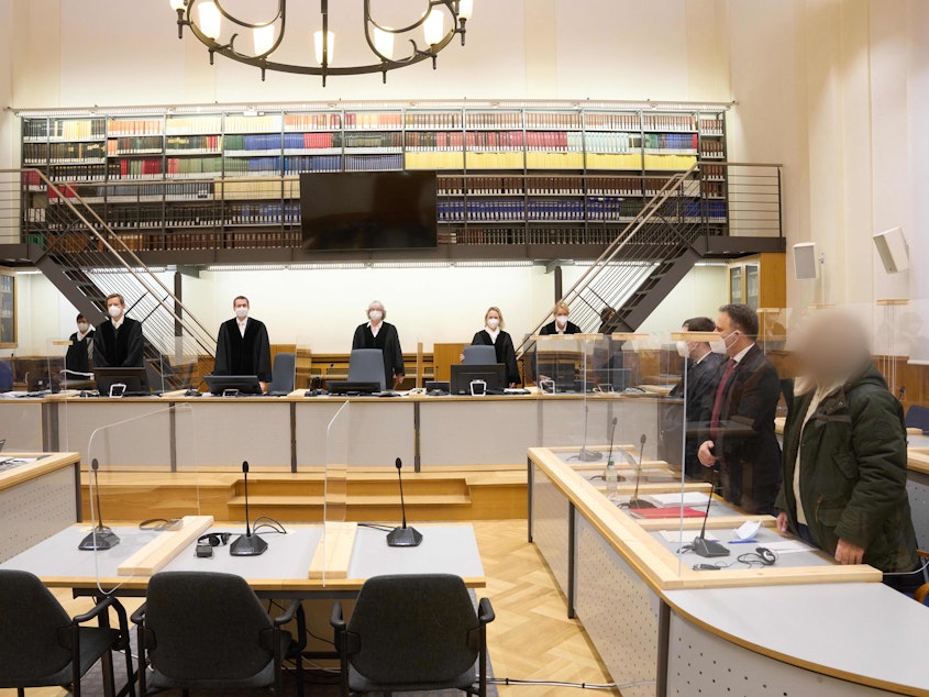 caption: Defendant Anwar Raslan (right) and others involved in his trial stand in the Higher Regional Court in Koblenz, Germany, at the start of a trial session last month. Raslan was put on trial in April 2020 in a landmark case in Germany.