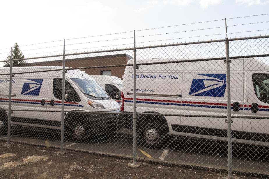 caption: United States Postal Service vans parked in a lot.