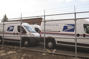 caption: United States Postal Service vans parked in a lot.