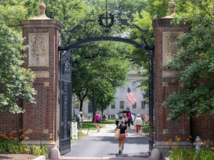 caption: CAMBRIDGE, MASSACHUSETTS - JUNE 29: People walk through the gate on Harvard Yard at the Harvard University campus on June 29, 2023 in Cambridge, Massachusetts.