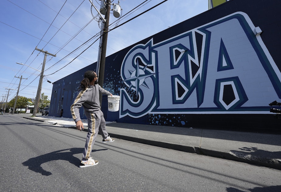 caption: Seattle Mariners shortstop J.P. Crawford throws paint balloons at a mural in SoDo on Saturday, April 23, 2022.