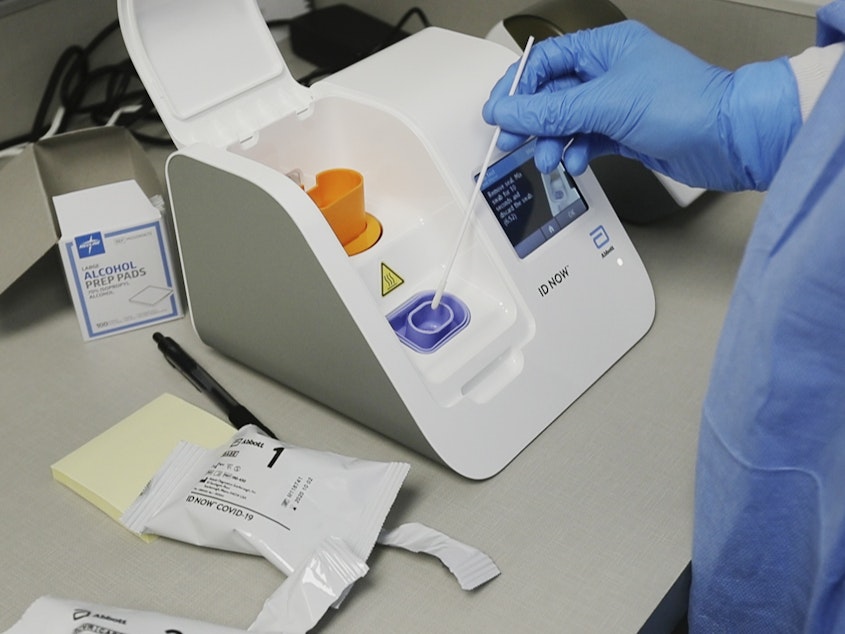 caption: A lab technician dips a sample into an Abbott Laboratories ID Now testing machine at the Detroit Health Center on April 10.