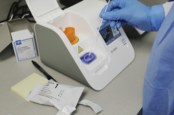 caption: A lab technician dips a sample into an Abbott Laboratories ID Now testing machine at the Detroit Health Center on April 10.