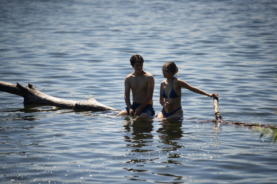 caption: Anthony Barbano, 18, left, and Sophie Egan, 18, cool off while sitting on a log in Lake Washington on Wednesday, July 27, 2022, at Seward Park in Seattle. 