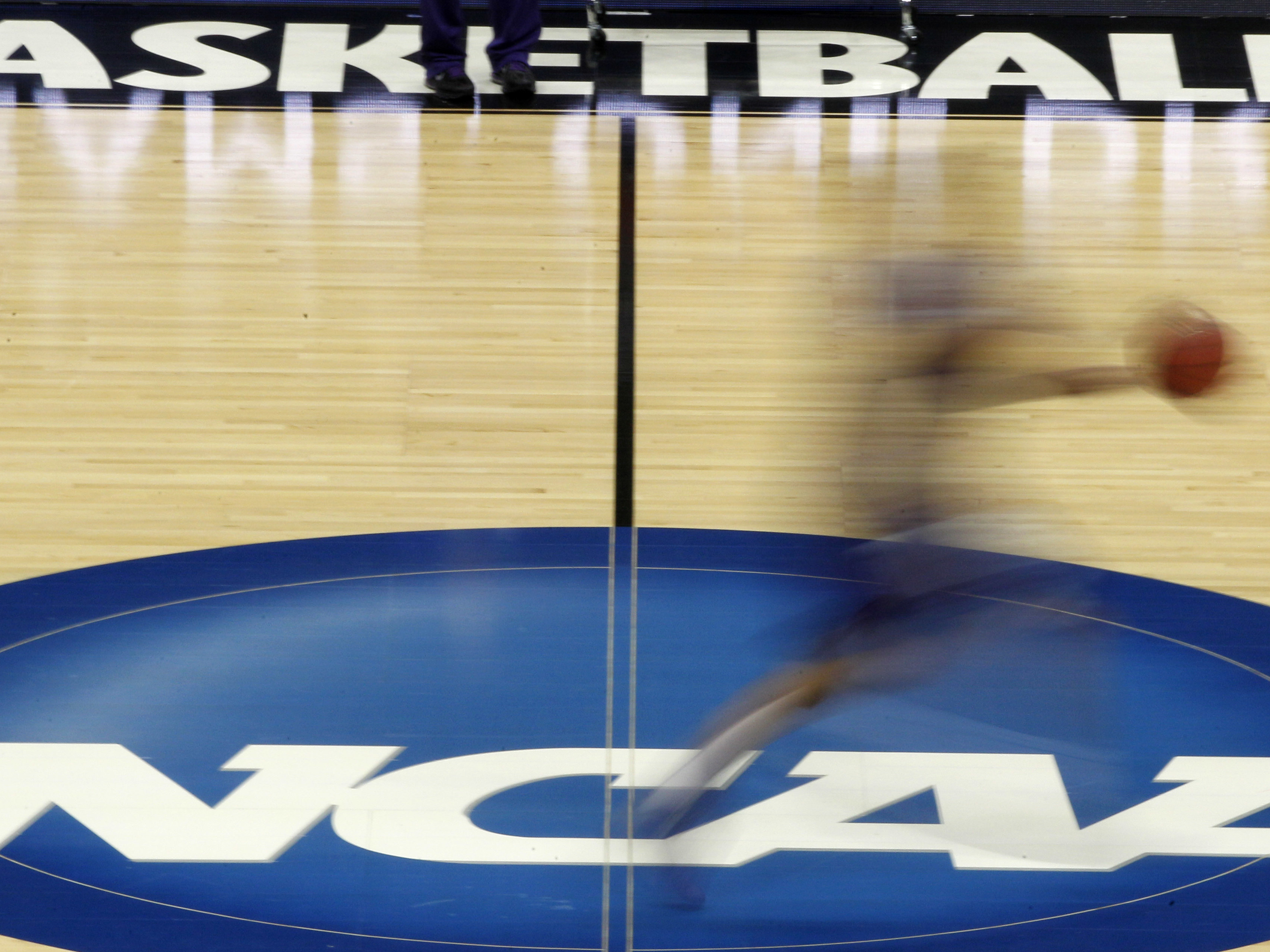 caption: A player streaks across the NCAA logo at midcourt during basketball practice in this file photo from March 14, 2012.