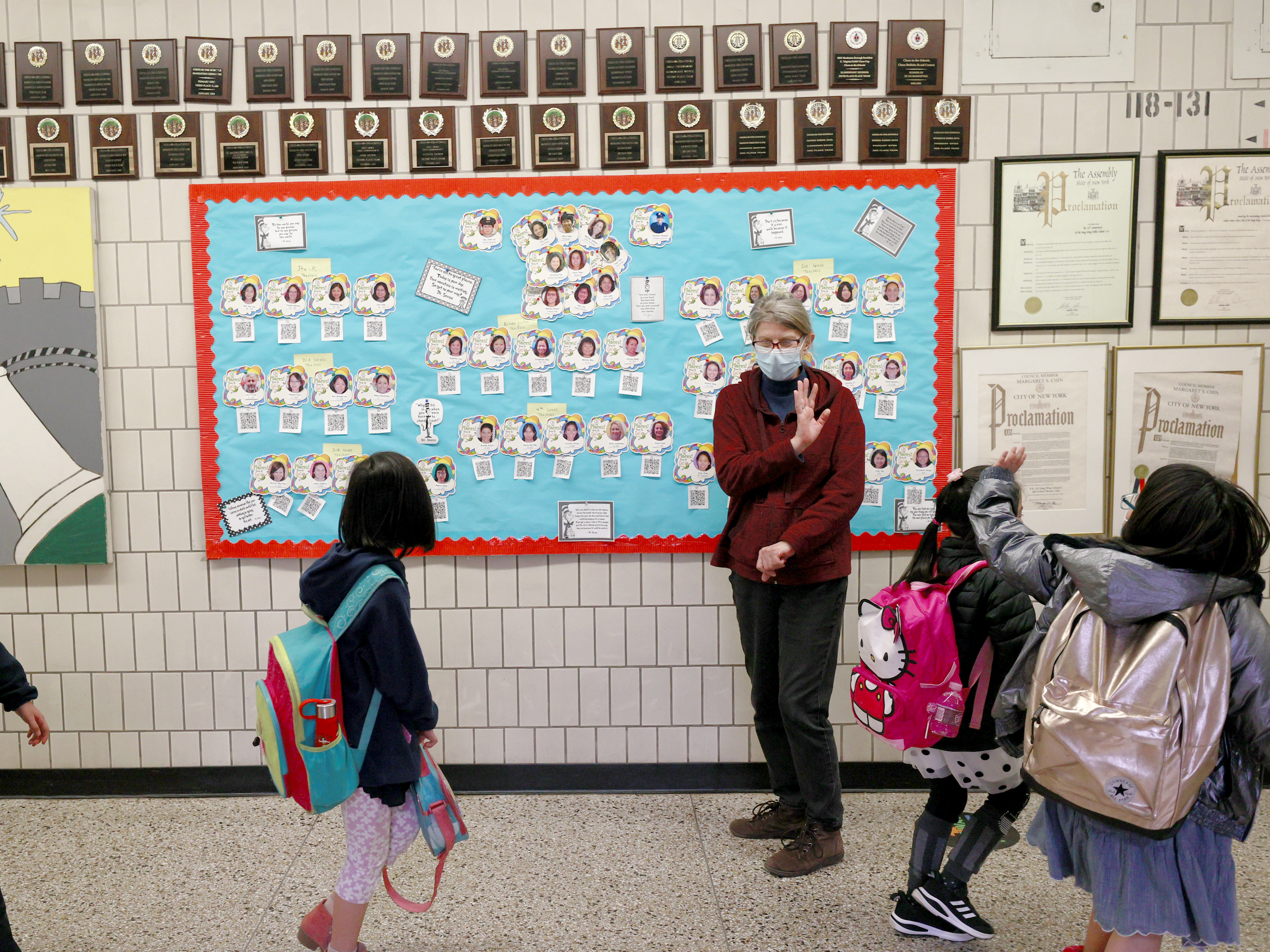 caption: Students wave goodbye during dismissal at Yung Wing School P.S. 124 on March 25, 2021 in New York City.