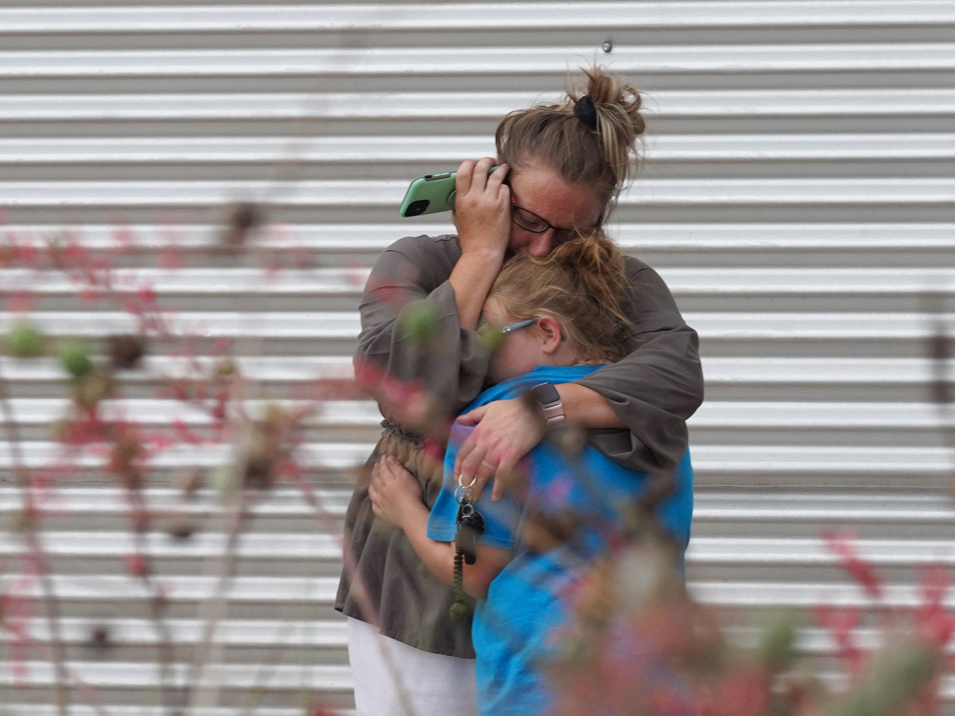 caption: A woman cries and hugs a young girl while on the phone outside the Willie de Leon Civic Center where grief counseling will be offered in Uvalde, Texas.