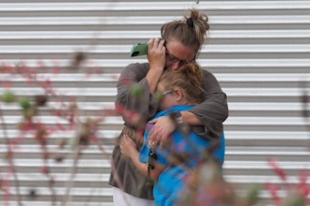 caption: A woman cries and hugs a young girl while on the phone outside the Willie de Leon Civic Center where grief counseling will be offered in Uvalde, Texas.