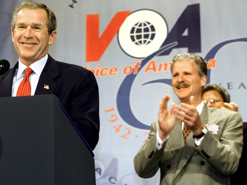 caption: Robert R. Reilly led Voice of America briefly under President George W. Bush. Here they're shown at a VOA anniversary celebration in February 2002.