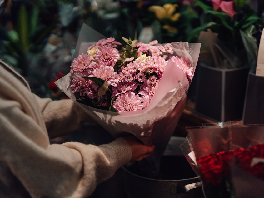 Cropped shot of young woman picking up a bouquet of fresh pink flowers in flower shop. She is buying flowers as a gift for her friends or for herself.