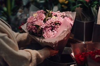 Cropped shot of young woman picking up a bouquet of fresh pink flowers in flower shop. She is buying flowers as a gift for her friends or for herself.