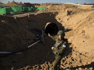 caption: Israeli military spokesman Rear Adm. Daniel Hagari stands at the opening to a tunnel near the border with Israel on Dec. 15, 2023, northern Gaza Strip. The Israeli military said this was the largest tunnel they'd found yet in Gaza.