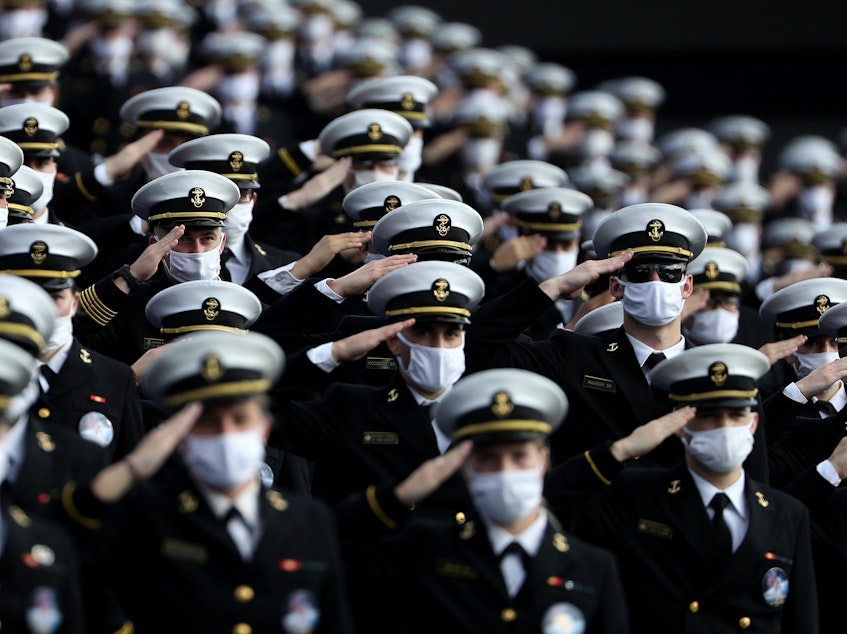 caption: Midshipmen wearing face masks stand and salute before the Navy Midshipmen play against the Houston Cougars on Saturday in Annapolis, Md. Researchers have tried to estimate how many lives would be saved by universal mask-wearing.