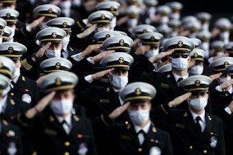 caption: Midshipmen wearing face masks stand and salute before the Navy Midshipmen play against the Houston Cougars on Saturday in Annapolis, Md. Researchers have tried to estimate how many lives would be saved by universal mask-wearing.