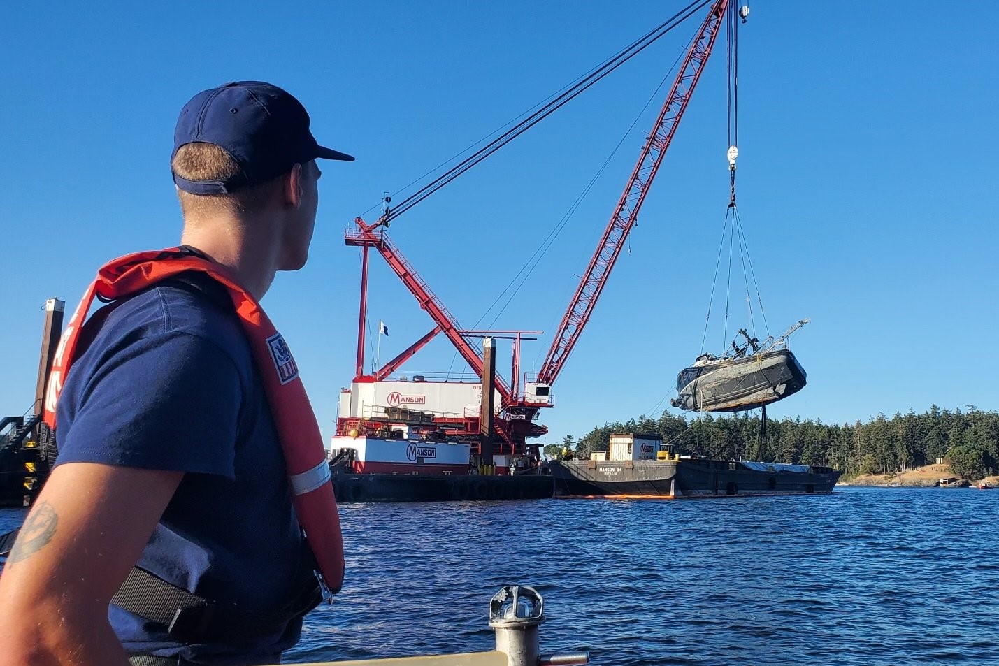 caption: A Coast Guard member watches the Aleutian Isle being lifted onto a barge off San Juan Island on Sept. 21.